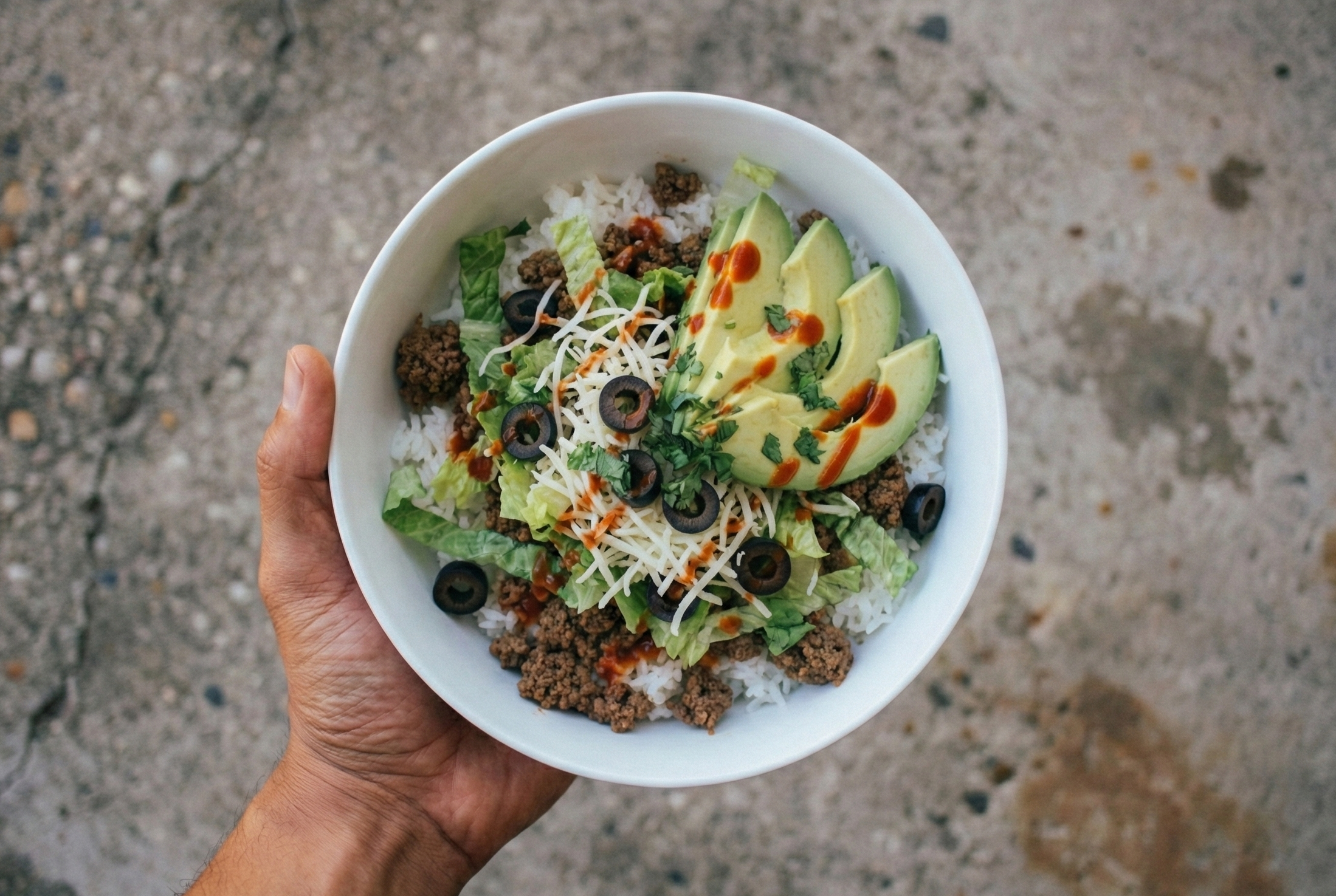 Overhead view of a beef taco bowl with basmati rice, shredded lettuce, cheese, and avocado